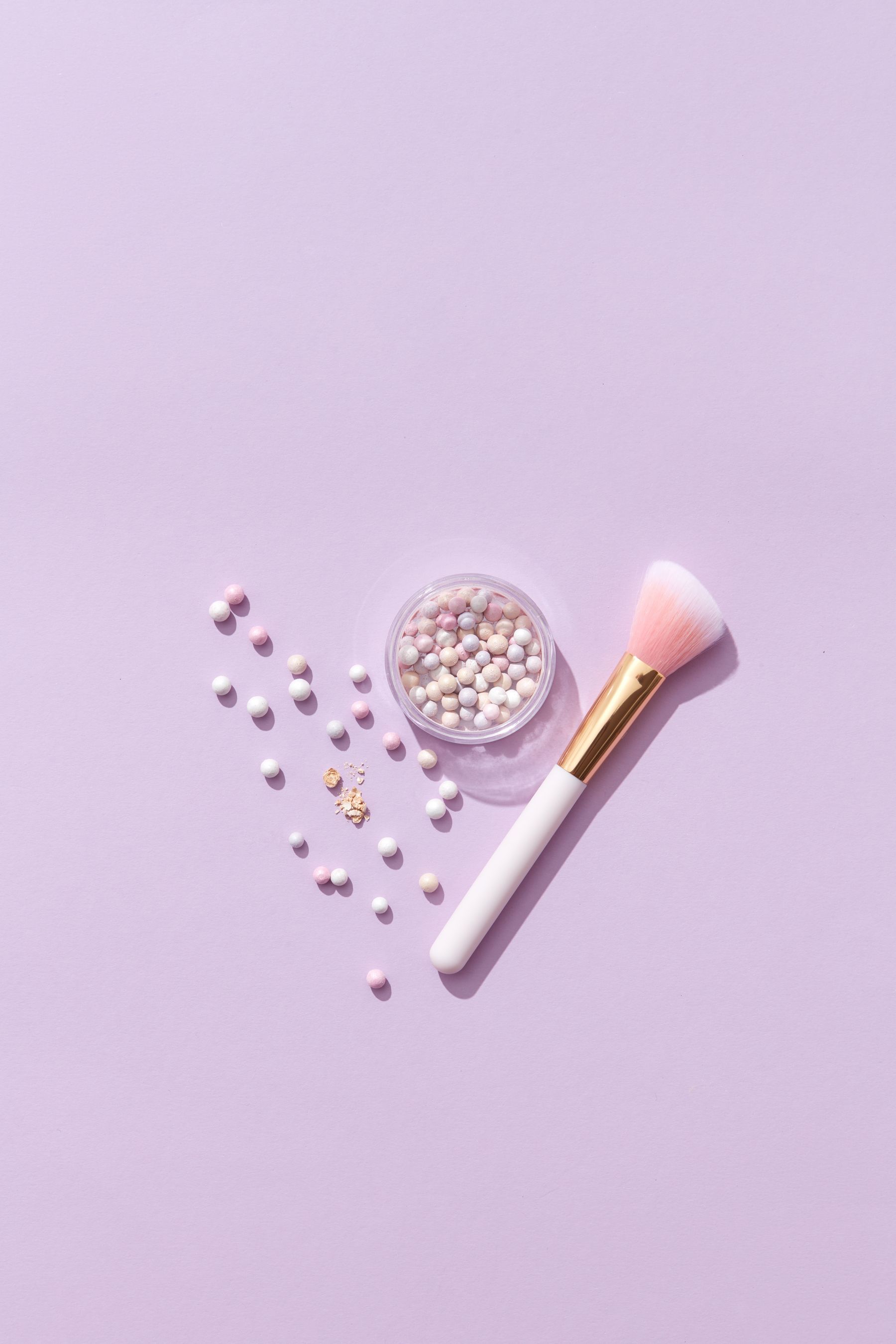 Makeup brush and cosmetic powder pearls on a lavender background
